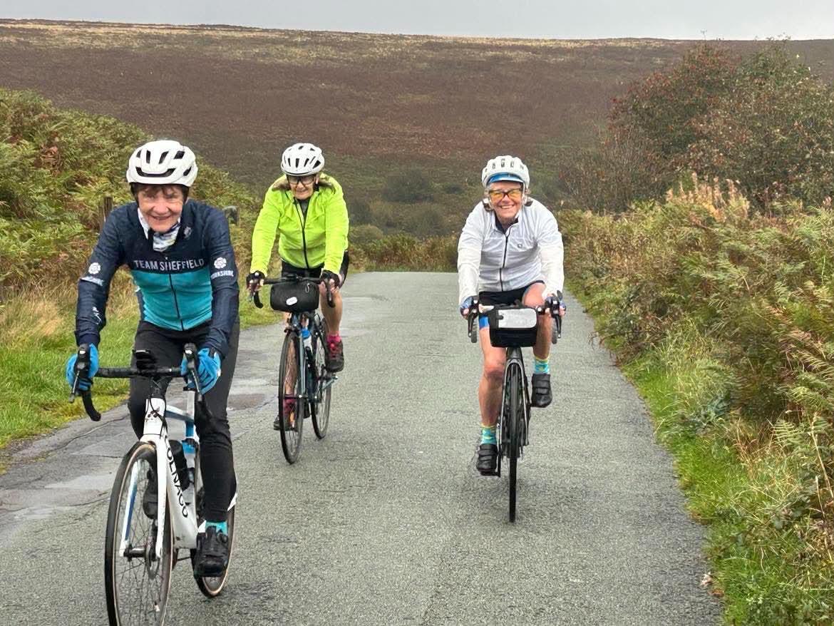 Three smiling cyclists riding together on a moorland road